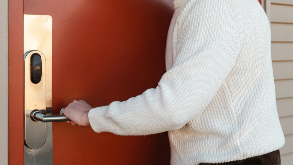 A person in a cream-colored sweater opens an orange door.
