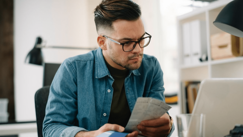 A man with glasses sits at a desk, looking intently at papers.