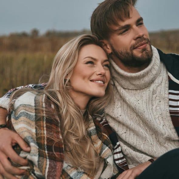 A couple sitting outdoors on a field, smiling and looking into the distance.