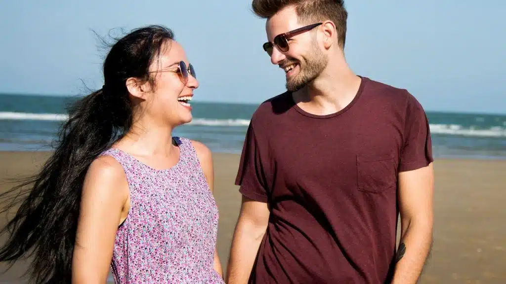 A couple laughing together while walking on the beach.