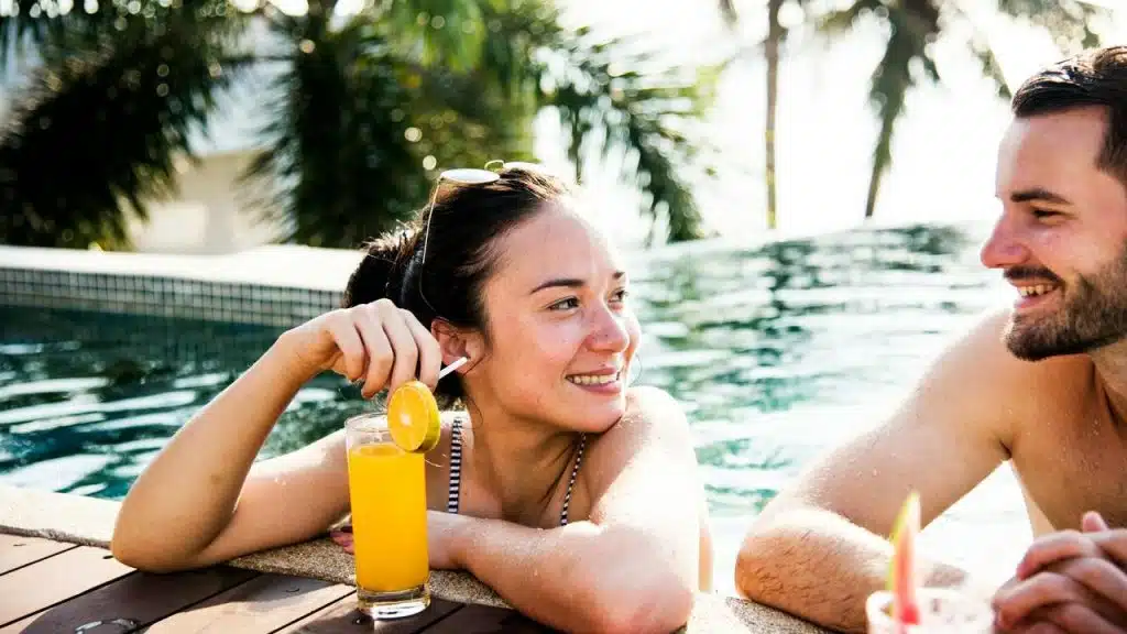 A couple relaxing by the pool, smiling and enjoying drinks.