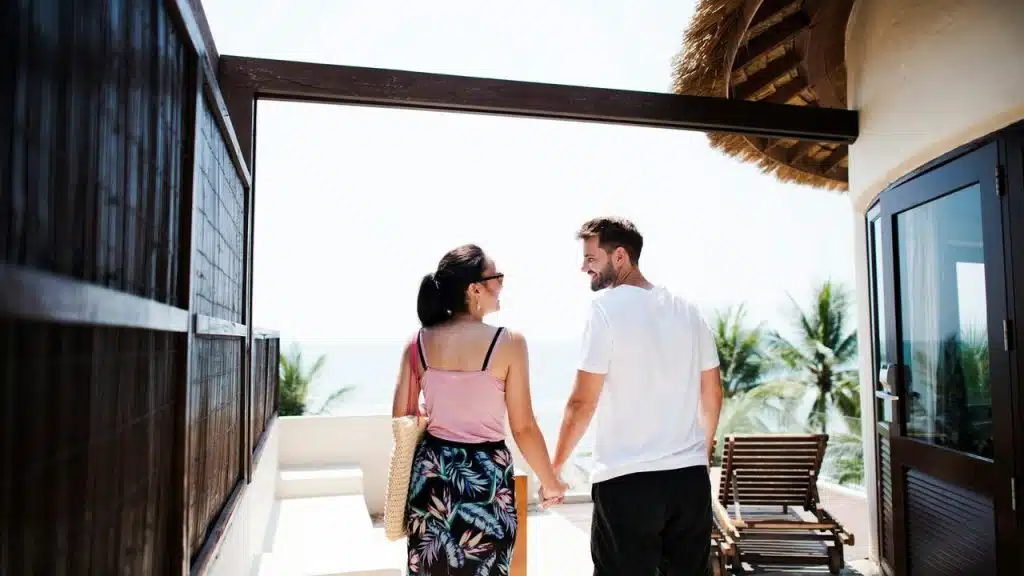 A couple holding hands and smiling while walking at a tropical resort.