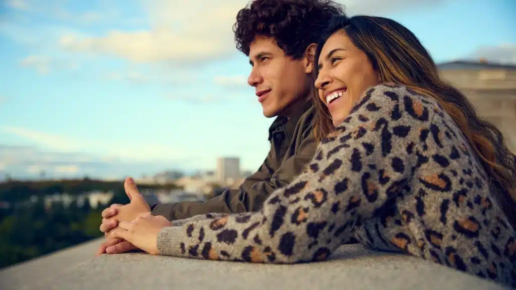 A couple leaning on a ledge outdoors, smiling and enjoying the view.