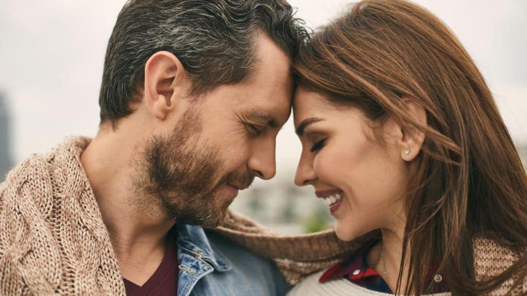 A couple standing close together with their foreheads touching, smiling warmly.