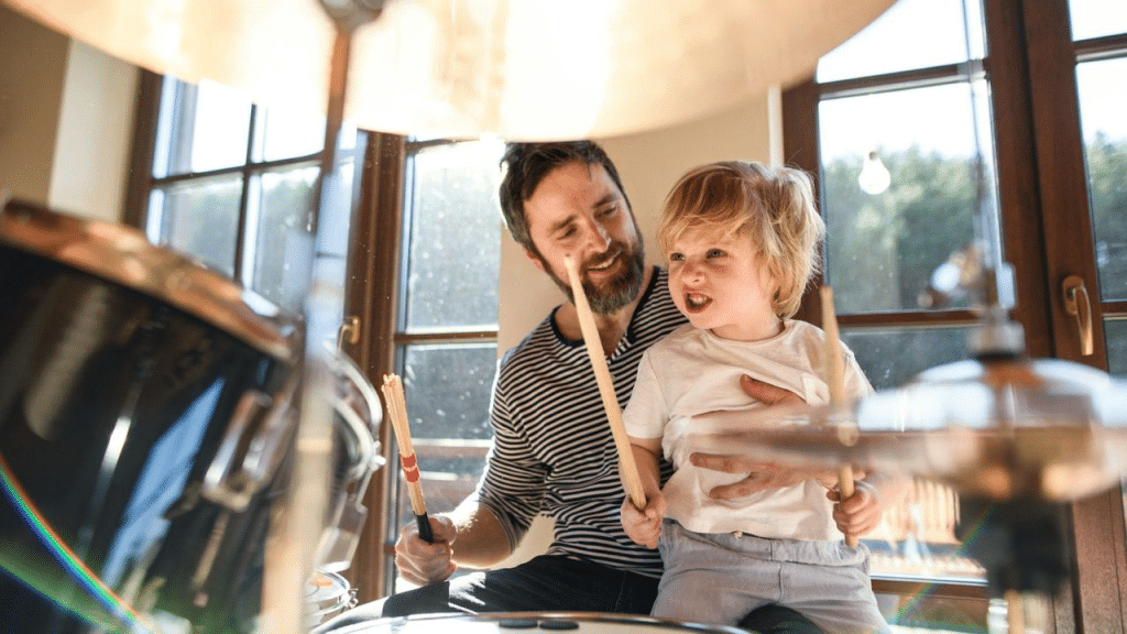 A man and a small child sit at a drum set together.
