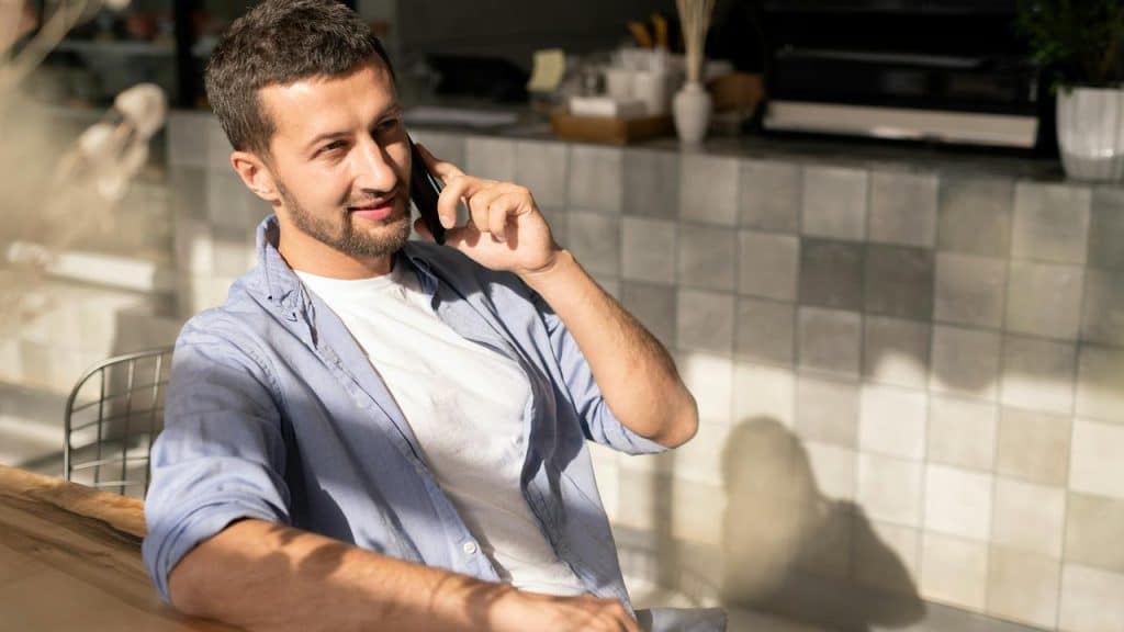 A smiling man sitting at a table talking on his phone.
