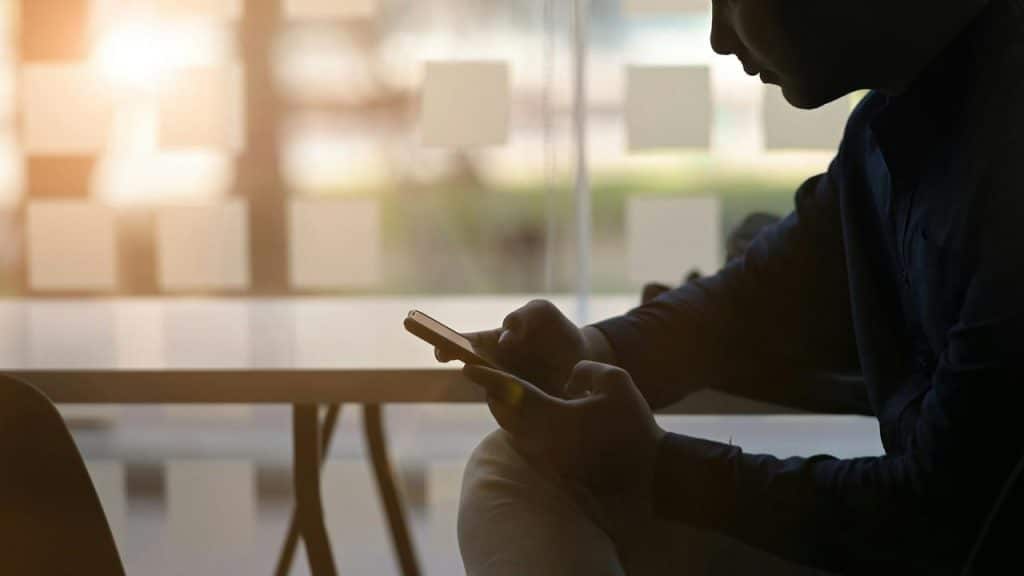 A man sitting indoors looking at his phone in low light.