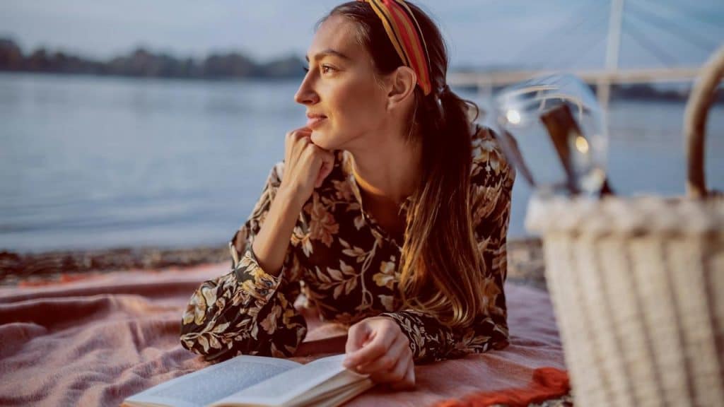 A woman lying by the water with an open book.