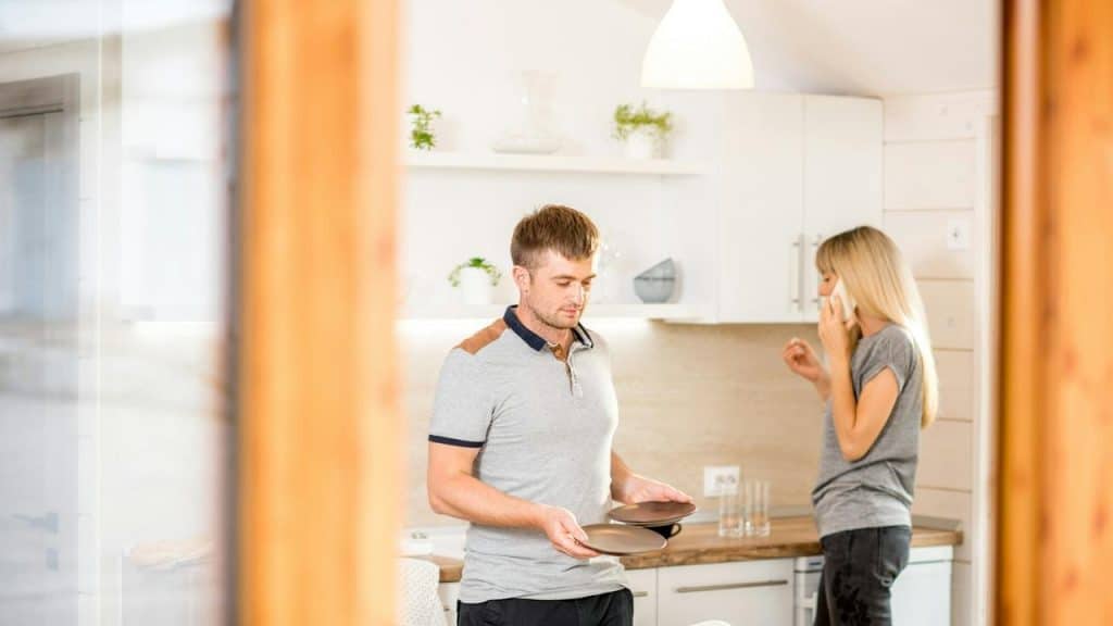 A man holding plates in a kitchen while a woman talks on the phone.