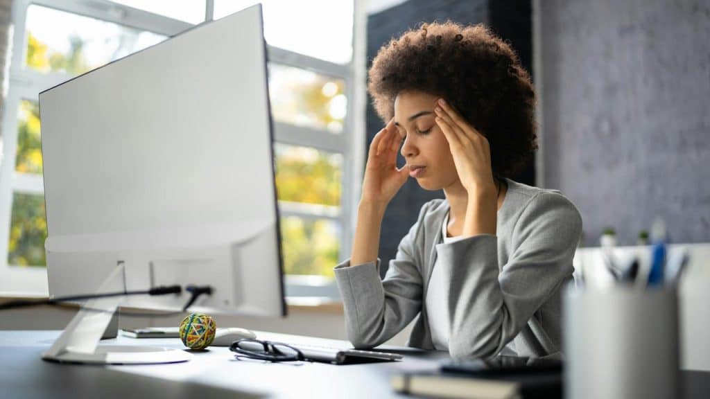 A woman at a desk with hands on her temples, looking stressed at a computer.