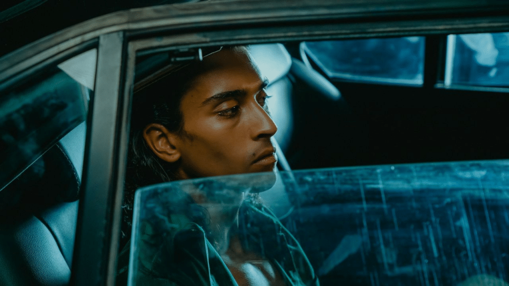 A man sits alone in a car at night, looking out the window.