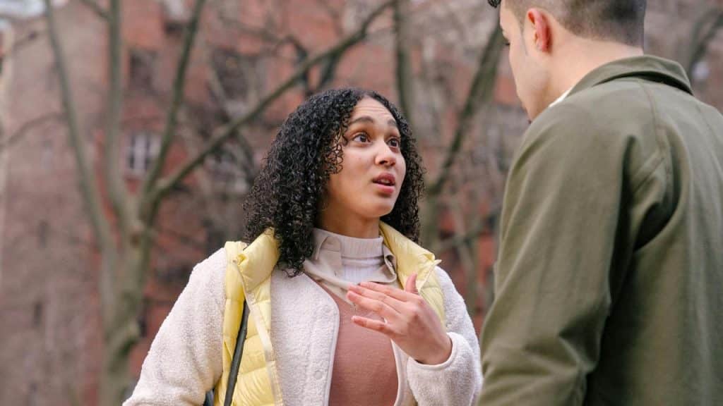 A woman speaking to a man outdoors with a concerned expression.