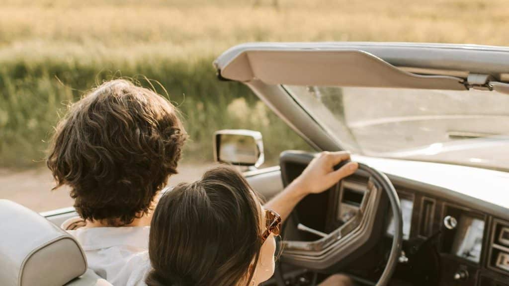 A couple driving in a convertible car on a sunny day.
