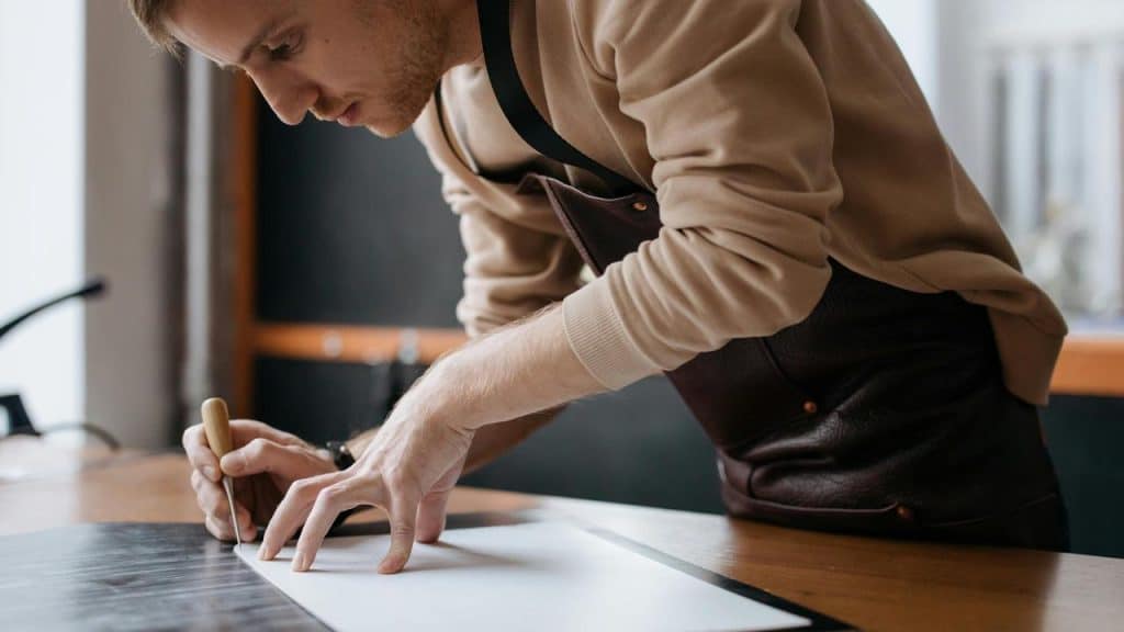 A man wearing an apron cutting material on a worktable.