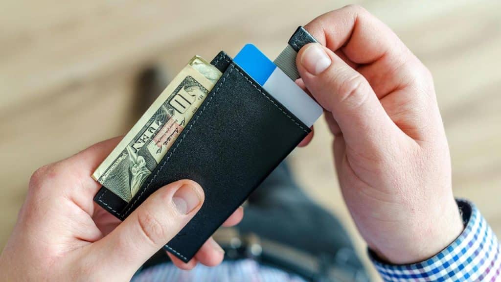 A person holding a slim black wallet with cash and credit cards.