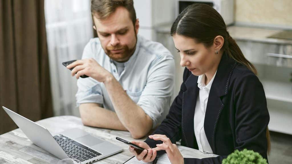 A man and a woman working together at a table with a laptop and a smartphone.