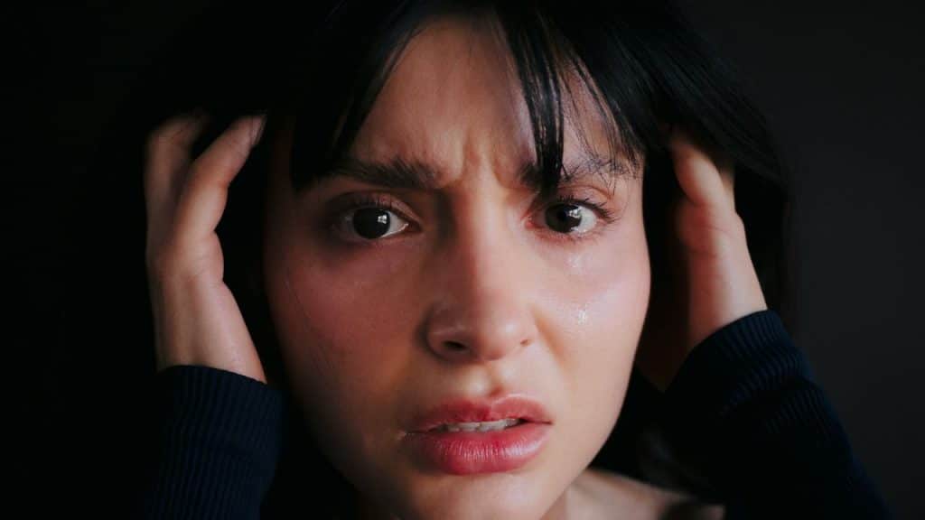 Close-up of a distressed person's face holding hands near their temples.