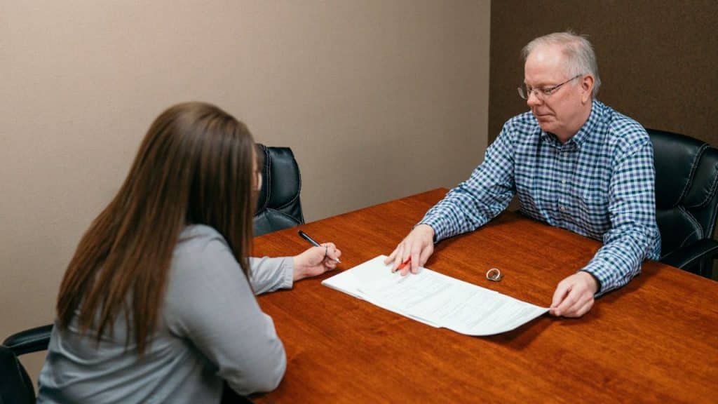 Two people sitting at a wooden table reviewing documents in an office.