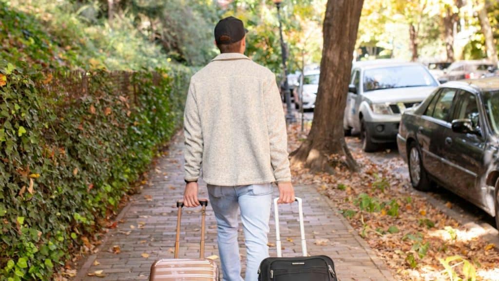 Person walks away on a sidewalk, pulling two roller suitcases behind them.