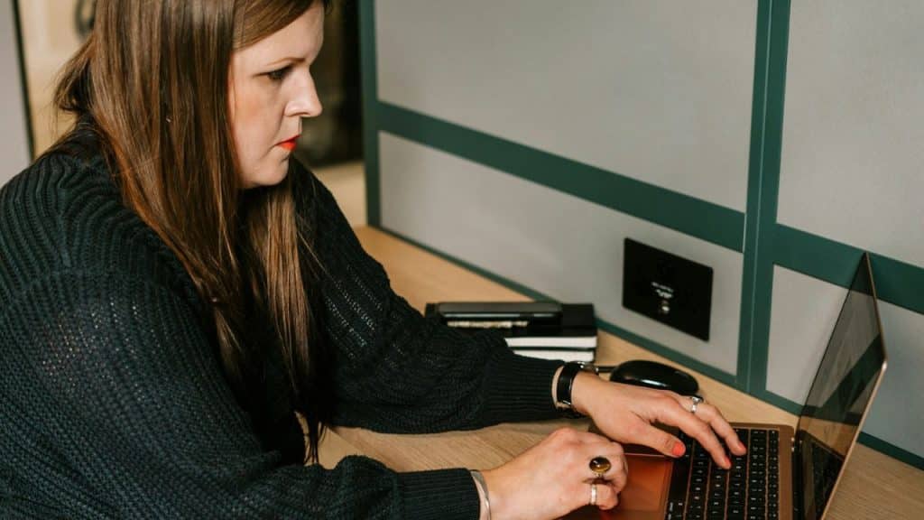 A woman with long brown hair intently typing on a laptop at a desk.