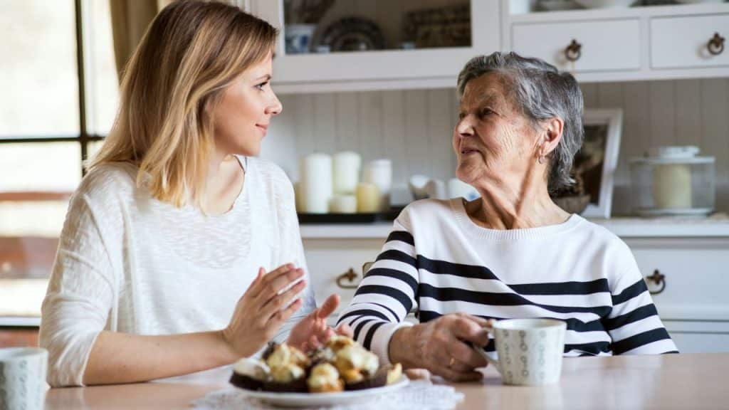 A younger woman talking to an older woman holding a mug, with pastries on the table.