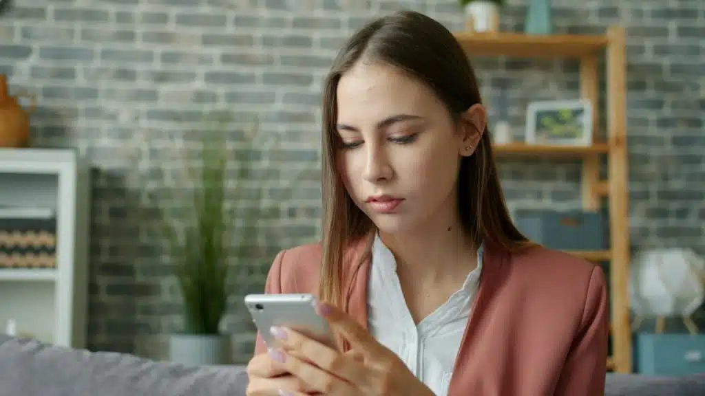 A young woman with long brown hair looks intently at her smartphone.