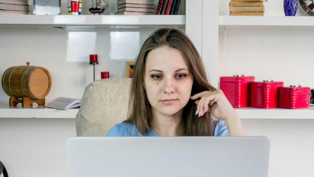 A young woman with long brown hair looks intently at a laptop screen.