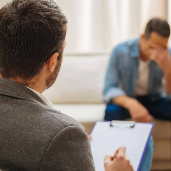 A man talking to a therapist while holding his head in distress.