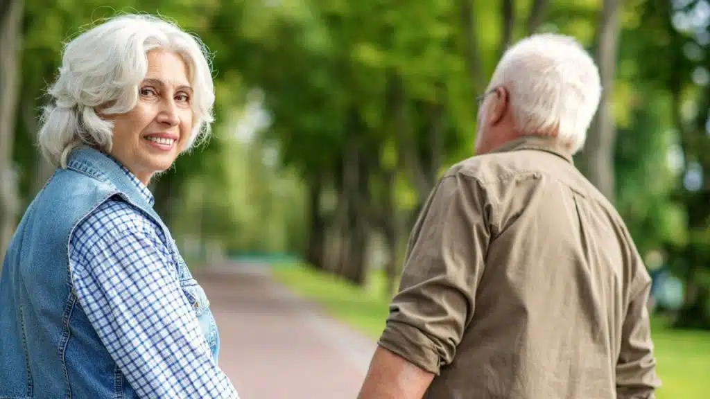 An older woman smiles over her shoulder while walking with a man in a park.