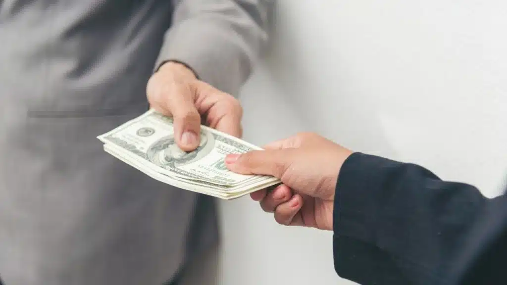 Two people exchange a stack of US srcset=