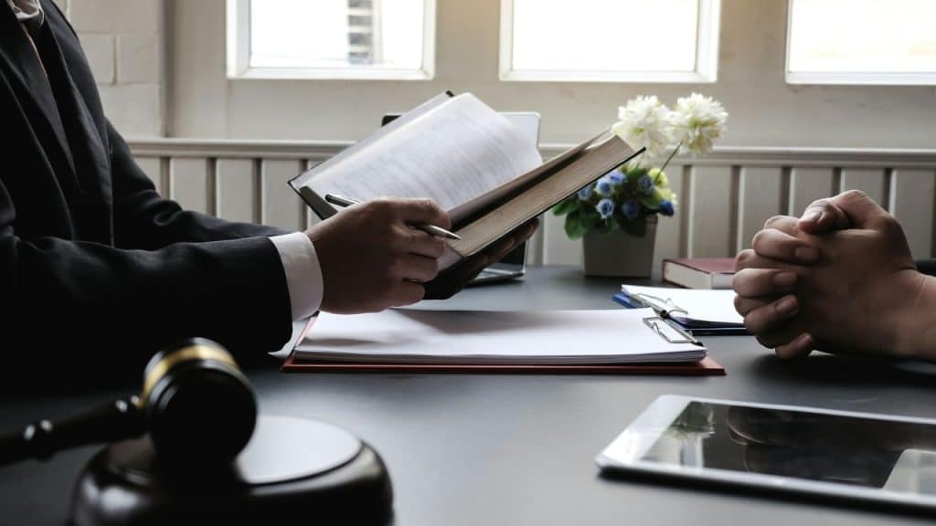 A lawyer in a suit reviews a document or book with a client in an office.
