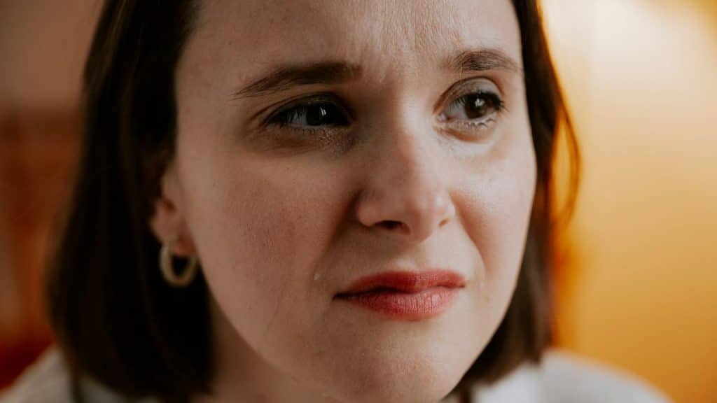 A distraught woman with tearful eyes looks away from the camera.
