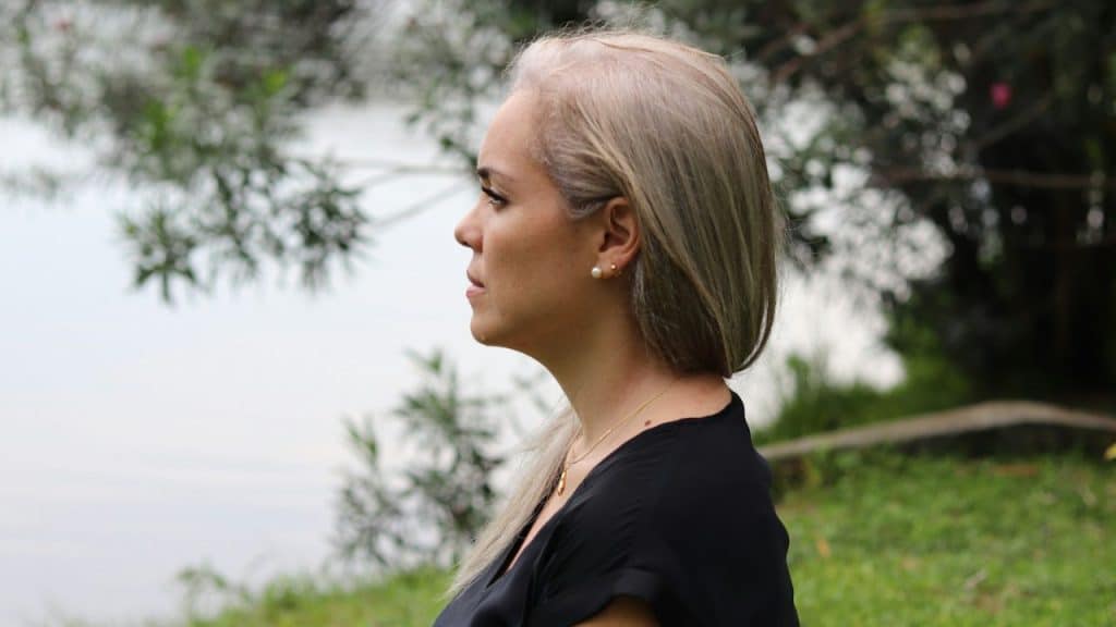 A middle-aged woman with blonde hair looks thoughtfully into the distance outdoors.