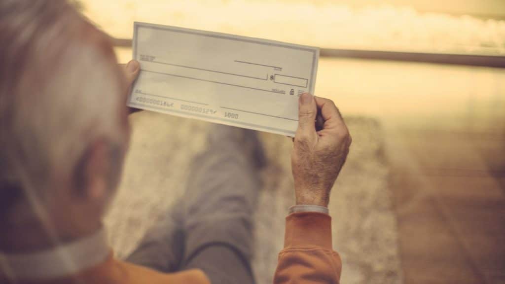 Elderly person's hands holding up a blank check, viewed over their shoulder.