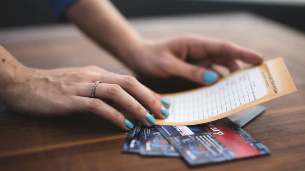 Woman's hands with blue nail polish holding a receipt or coupon over a stack of loyalty cards.