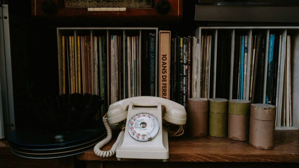 A vintage rotary telephone sitting on a shelf in front of a collection of records and books.