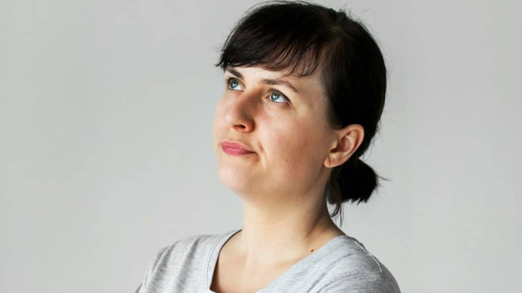 Close-up of a woman with dark hair looking up against a plain gray background.