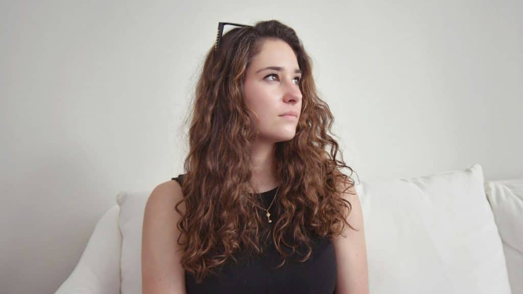 A young woman with long curly hair looks to the side on a white sofa.