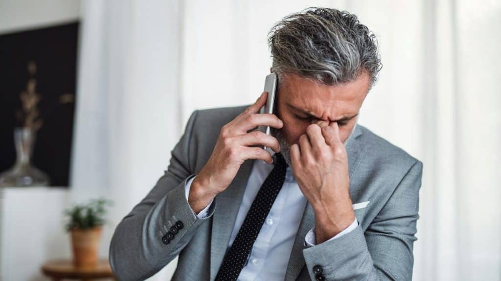 A stressed businessman talking on the phone while rubbing his eyes.