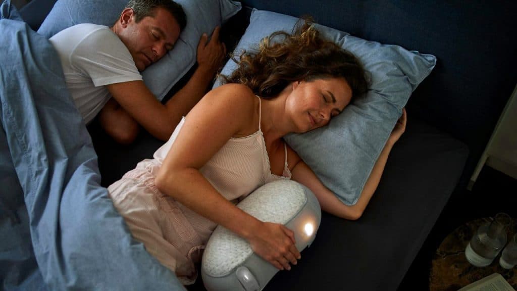 A man and woman sleep separately while she holds a light-up gray pillow.