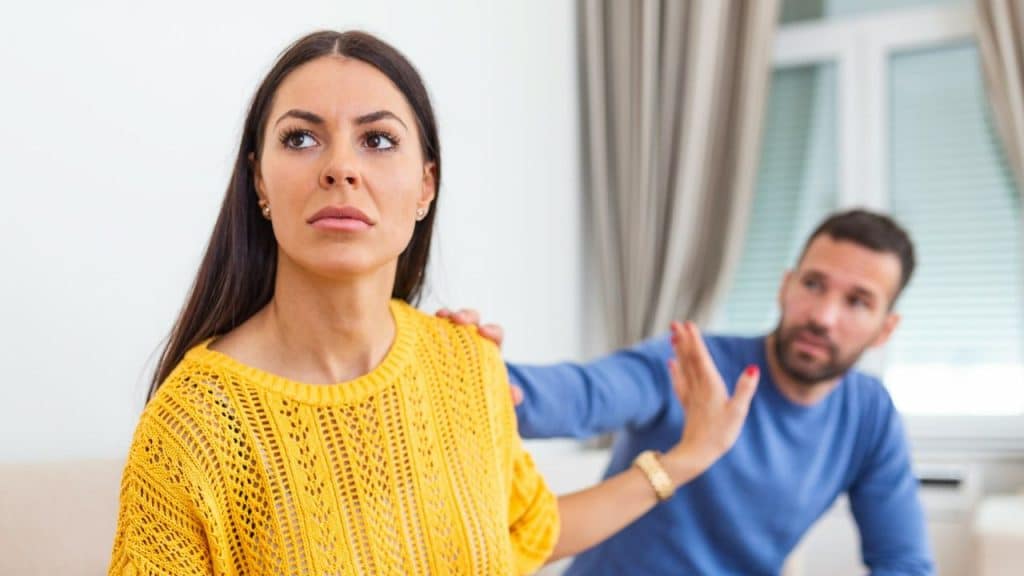 A woman in yellow looks away while a man gestures at her from behind.