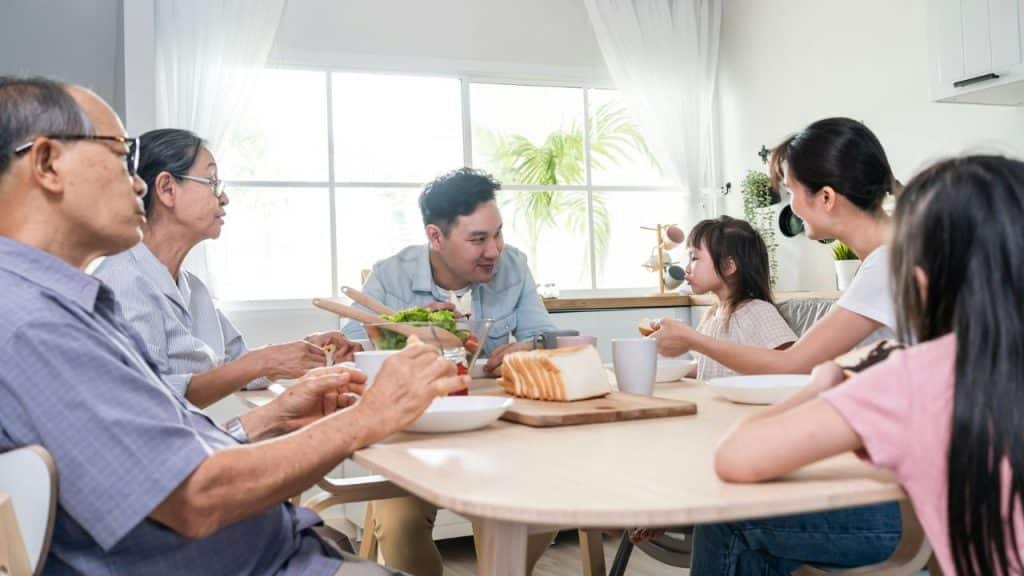 A multi-generational Asian family is gathered around a table having a meal indoors..