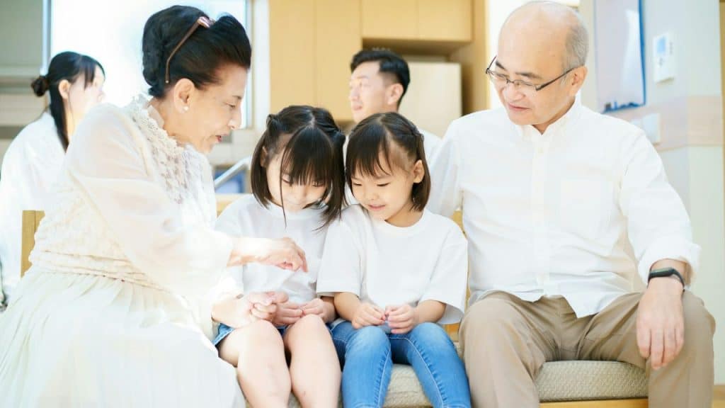 An Asian grandparent couple is sitting with two granddaughters in a bright, modern room.