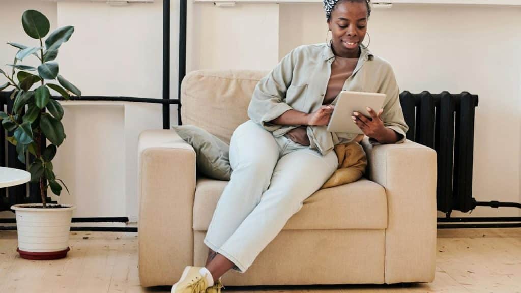 A woman sitting on a beige armchair using a tablet.