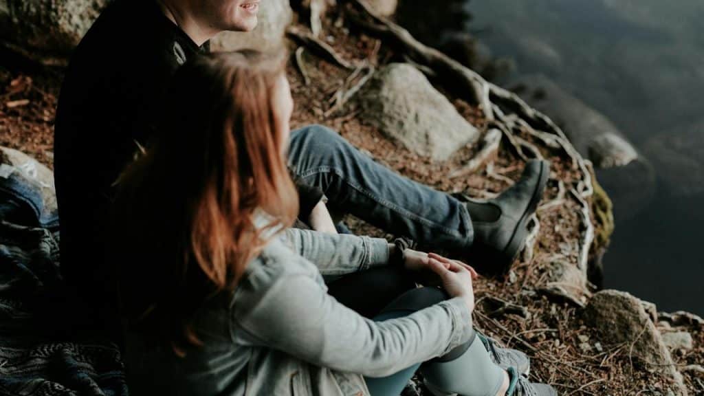 A couple sitting on a rocky lakeside.