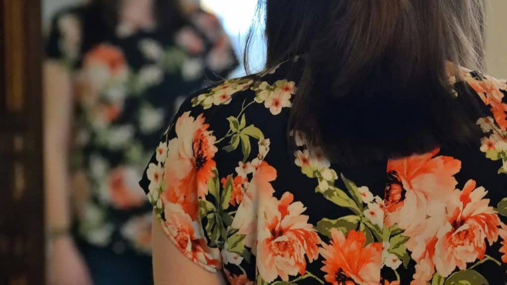 A woman in a floral shirt looking at her reflection in a mirror.