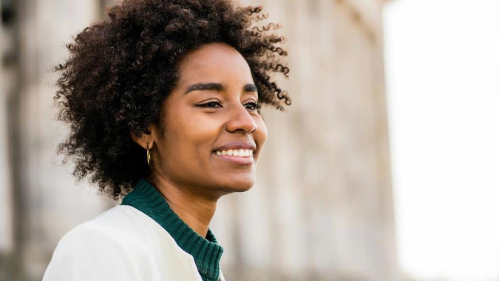A smiling woman with curly hair standing outdoors.