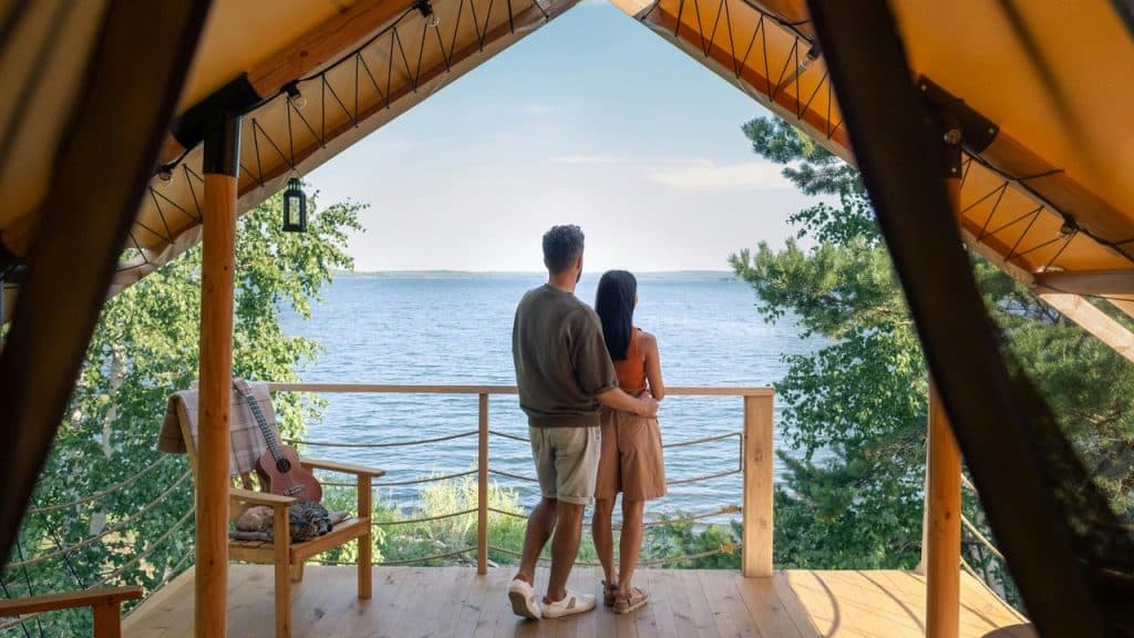 A couple standing on a wooden cabin balcony overlooking a lake.