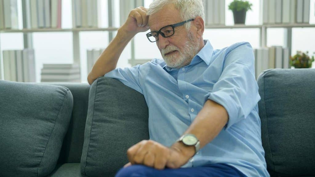 An older man sitting on a couch looking worried.