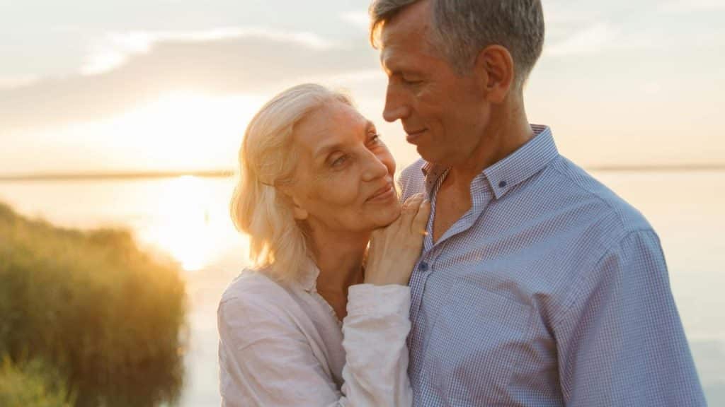 A senior couple embracing by a lake at sunset.